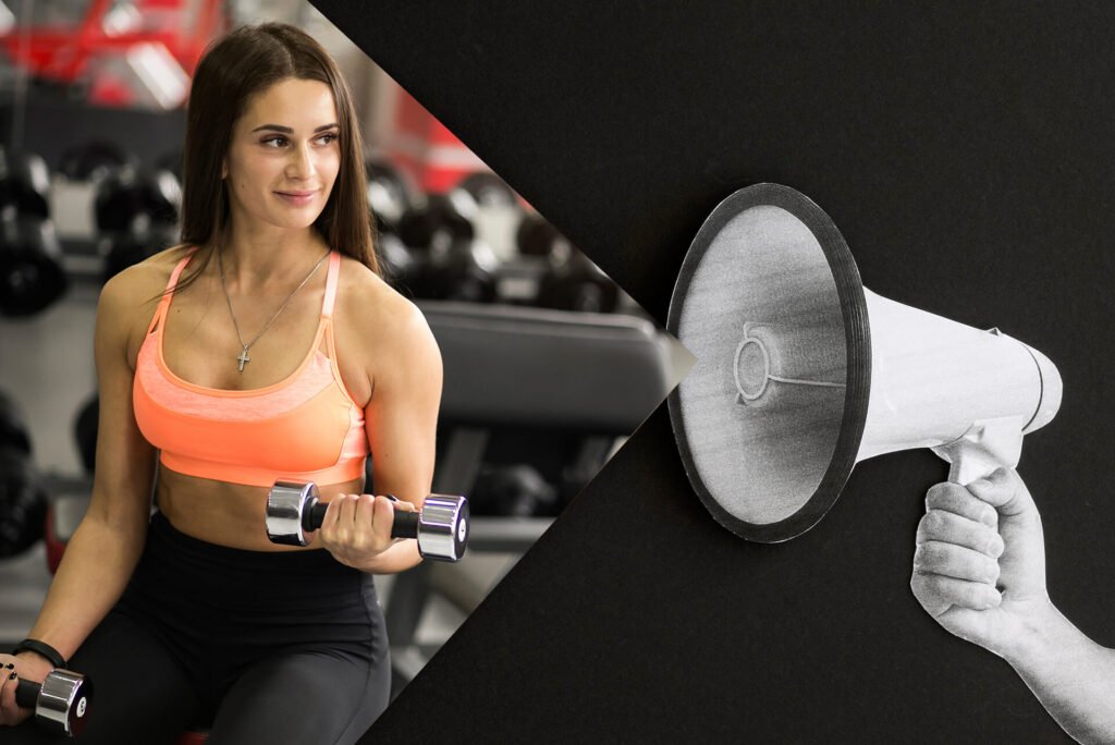 A smiling woman sitting on a bench in the gym, holding dumbbells, with a hand holding a megaphone on the right side.